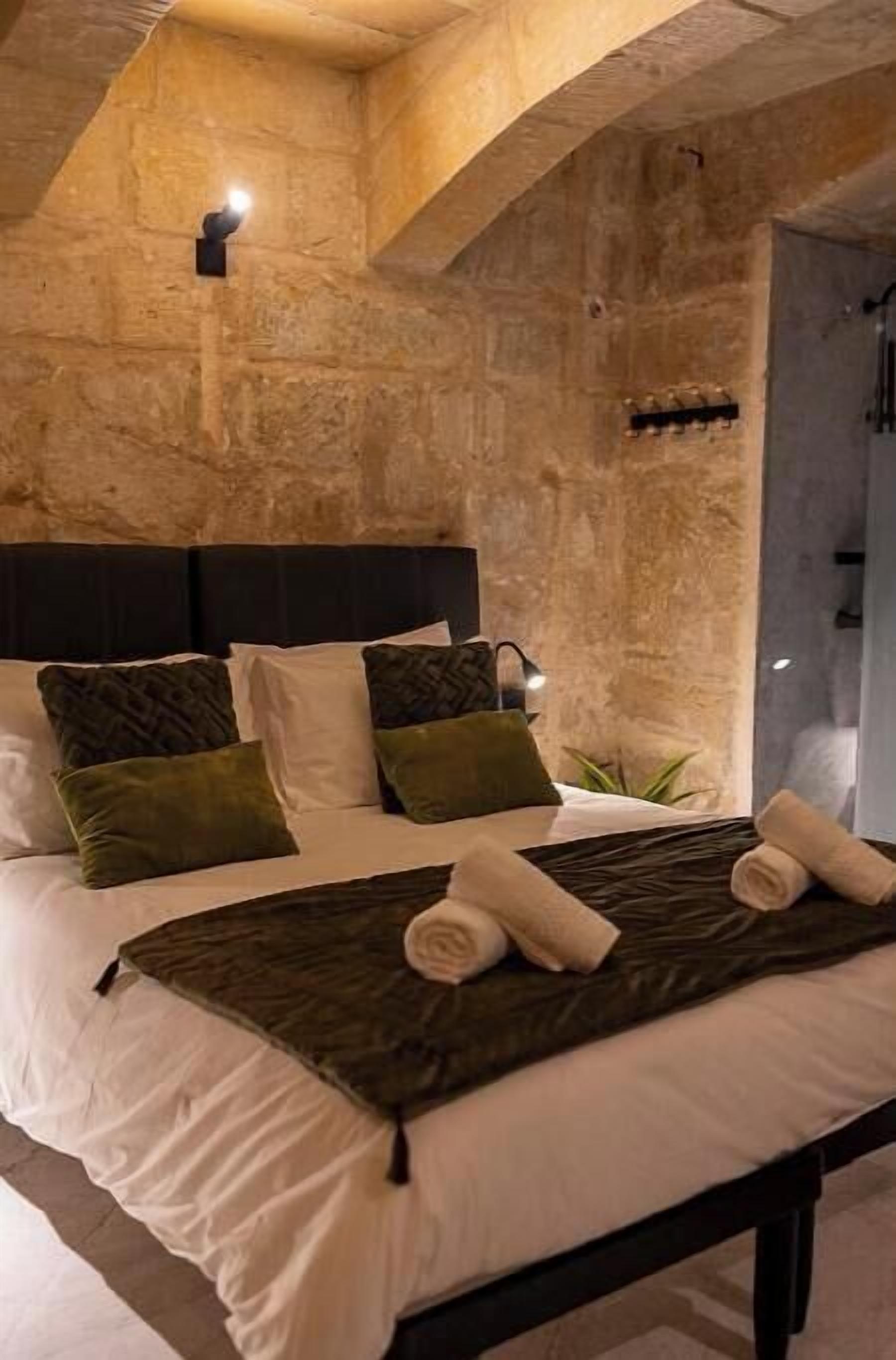 Un dormitorio con pared de piedra, cama con ropa de cama blanca y verde, y cabecera.
