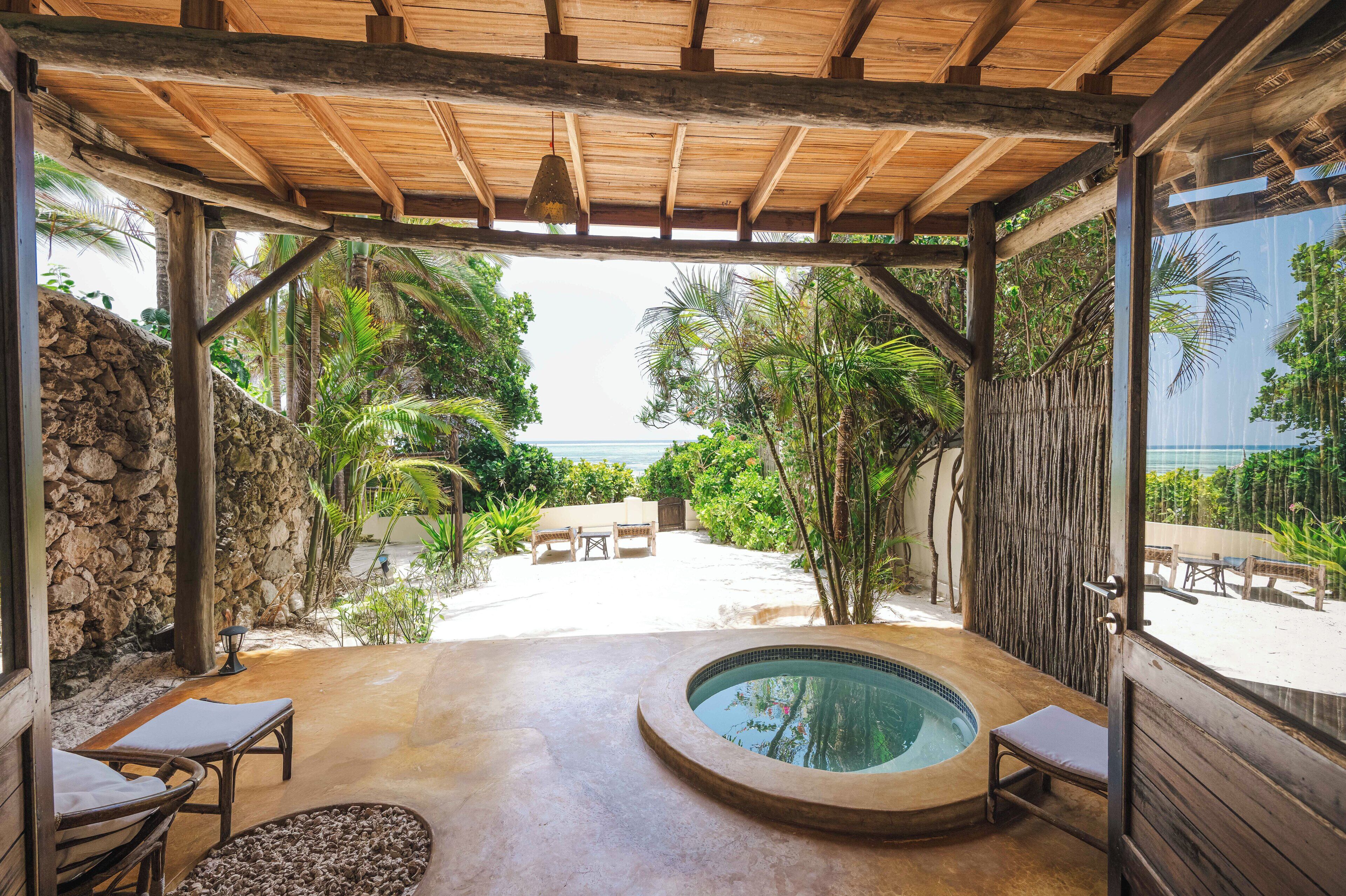 Un espacio al aire libre techado con un jacuzzi, sillones de descanso y vistas a la playa.