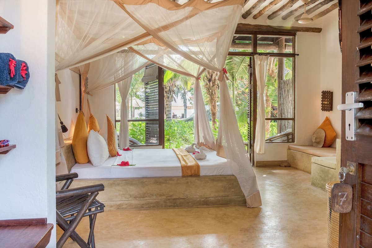 Quarto com cama sob dossel, um banco e vista para o verde lá fora.