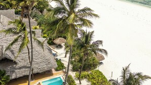 Un complexe hôtelier en bord de mer, doté d’une piscine, de palmiers et offrant une vue sur l’océan.