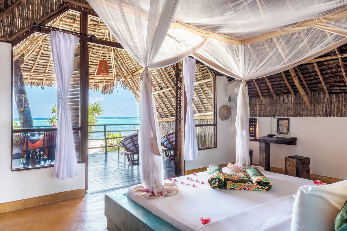 Quarto com cama, ventoinha, mesa pequena e vista para o oceano.