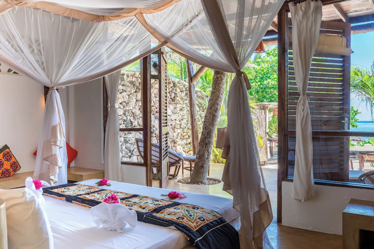 Quarto com cama, dossel, parede de pedra e vista para o exterior.