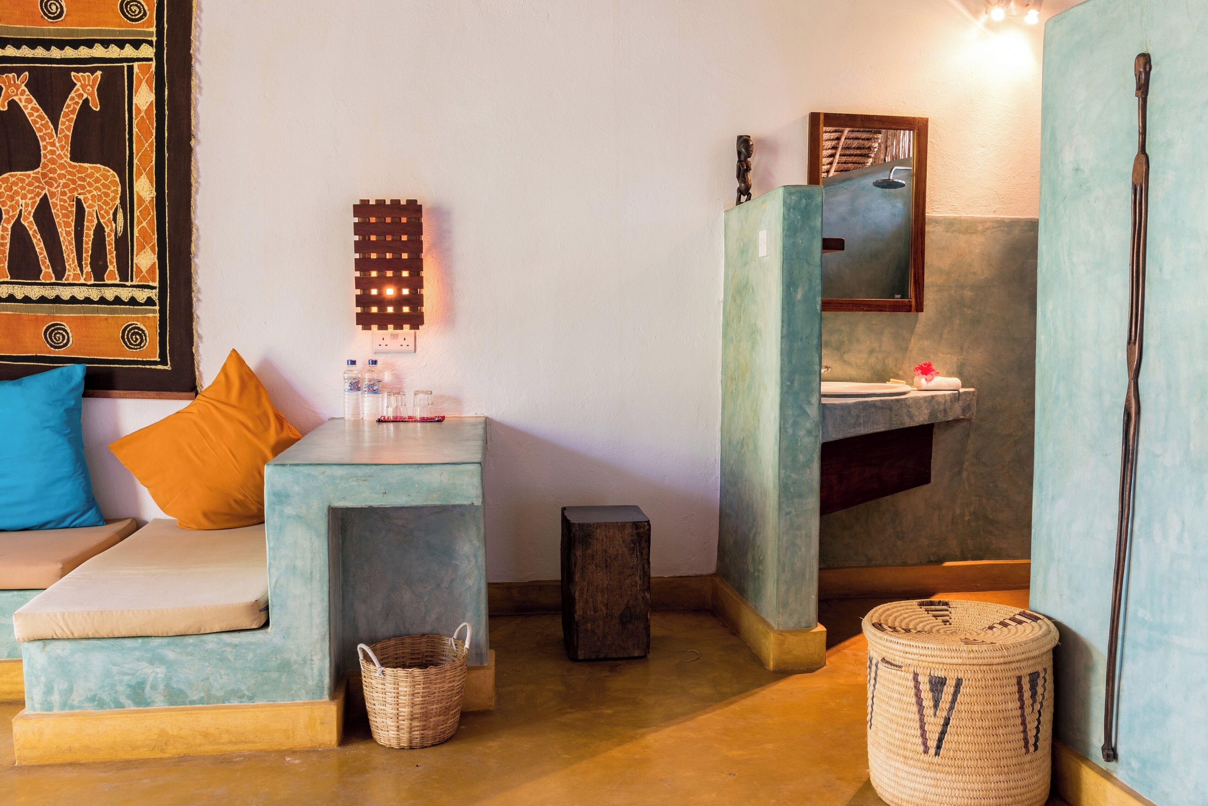 A room with a sofa, a small table with a basket, a wall-mounted light fixture, and a mirror above a sink.