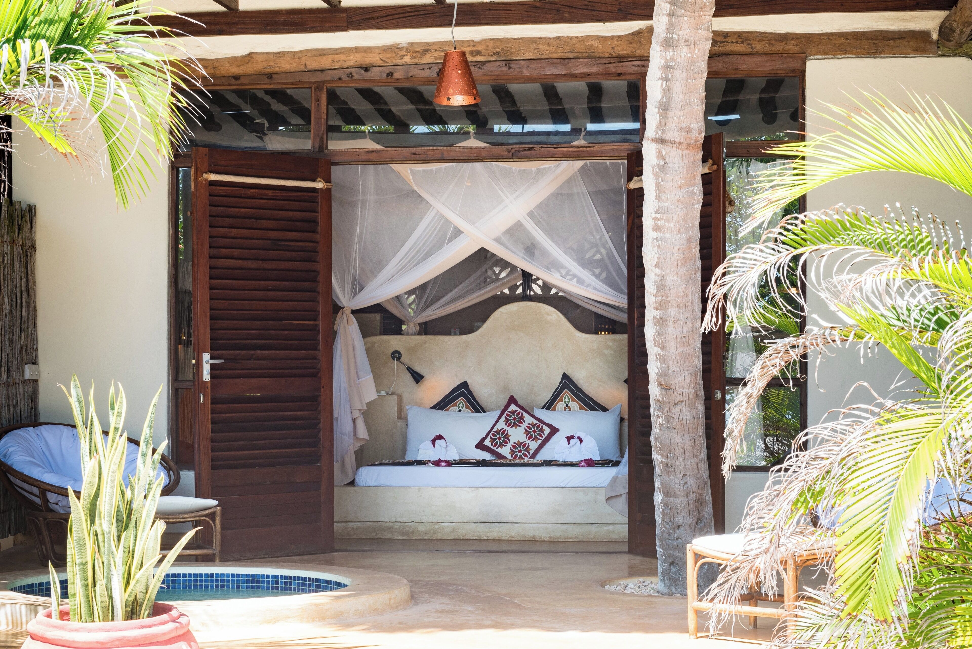 A bedroom with a bed, a mosquito net, and a view of a pool.