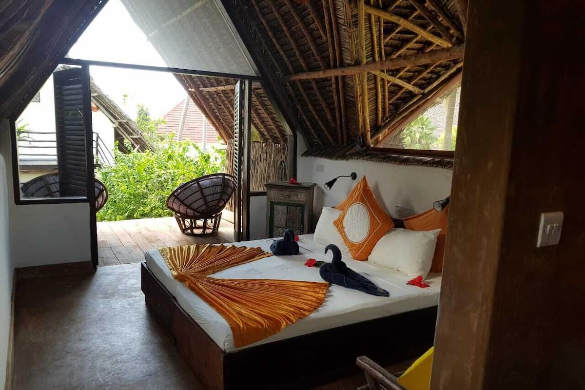 Quarto com cama, cadeira, mesa de cabeceira e janela.