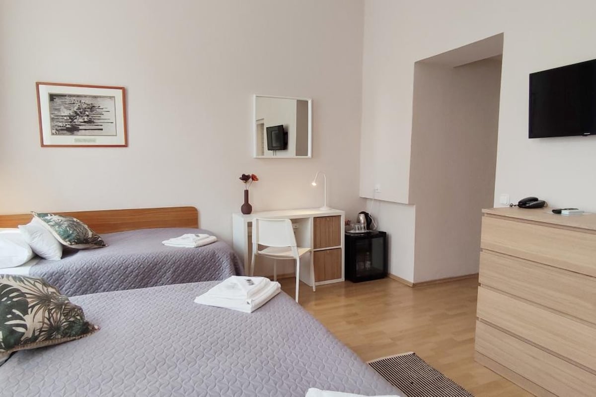 A hotel room with two beds, a desk, a chair, a TV, and a dresser.