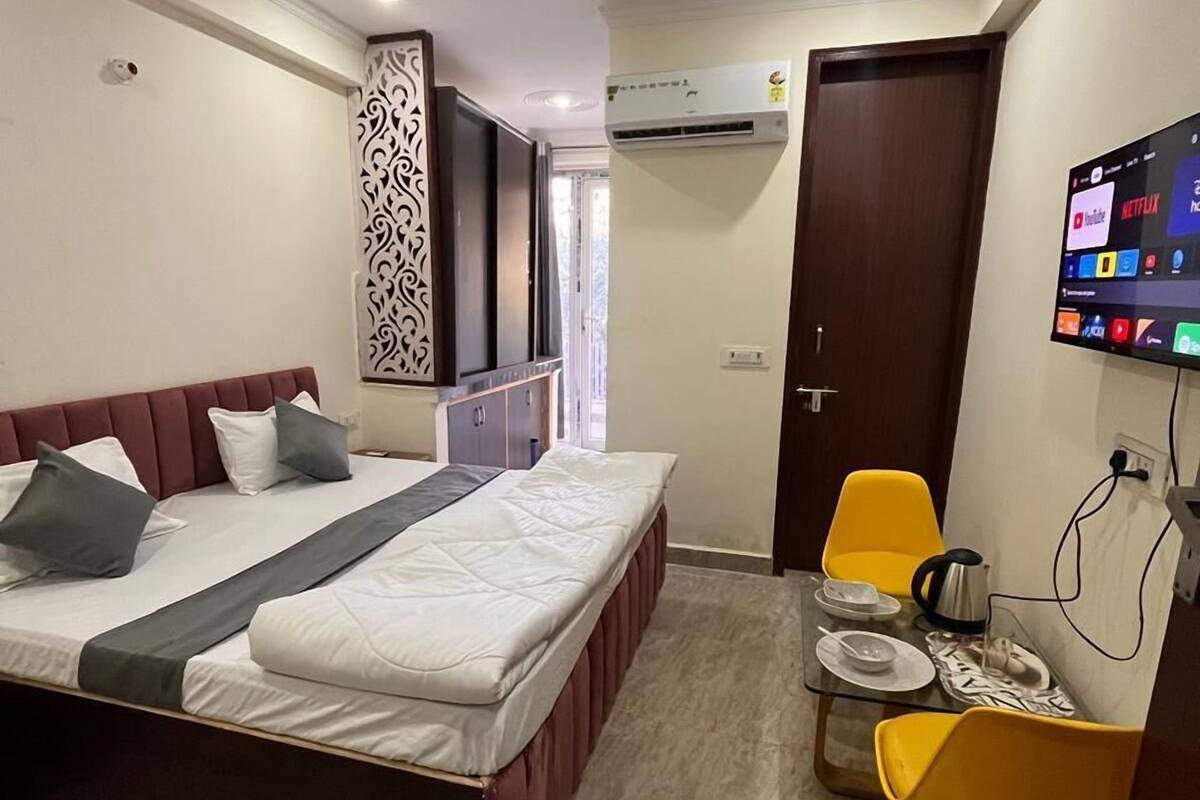 A modern hotel room with a bed, a desk, a chair, an air conditioning unit, and a television.