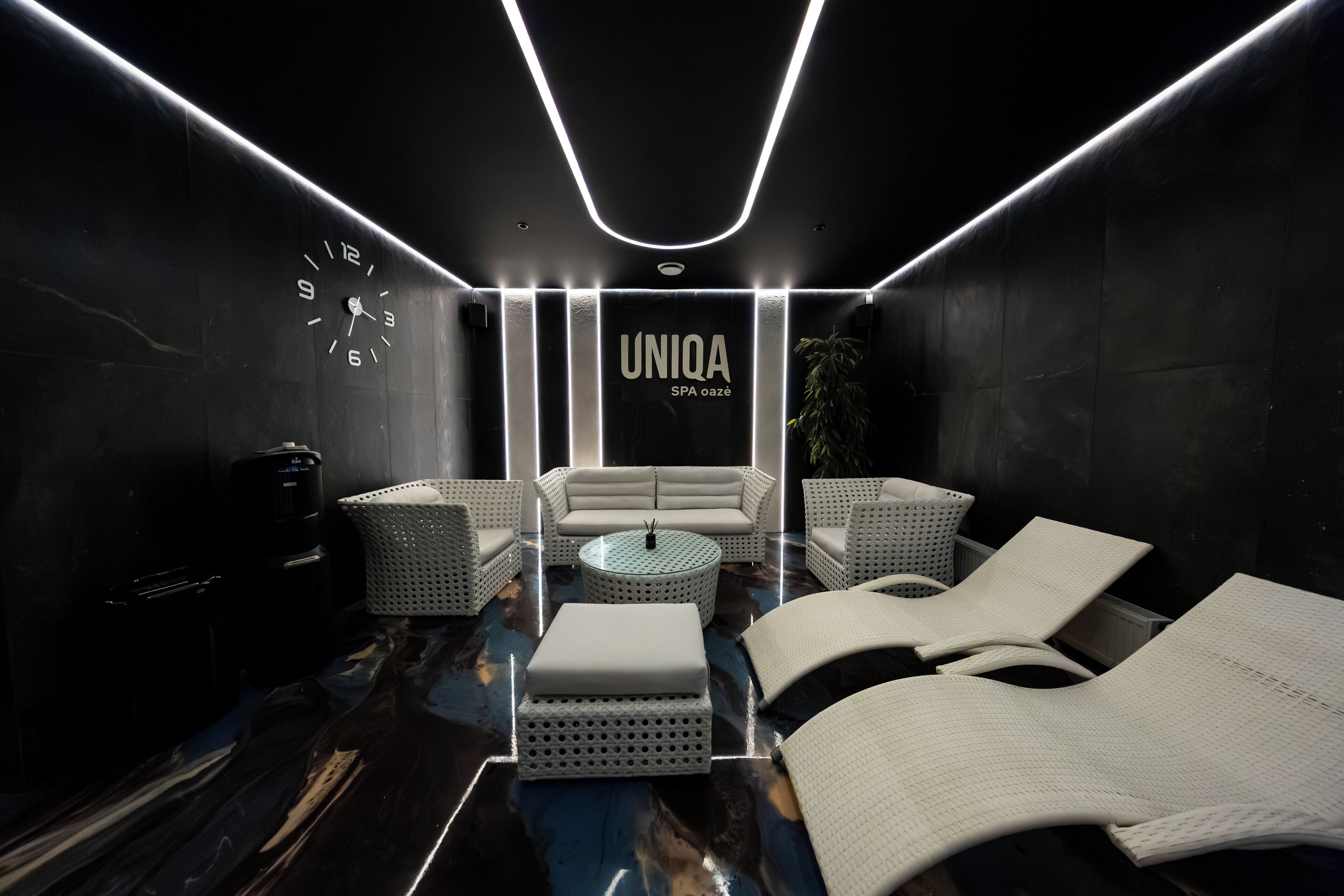 Une salle de spa moderne, équipée d’un canapé, de fauteuils, d’une table basse et d’une horloge murale.