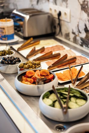 Un bufé con diversos alimentos, como aceitunas, tomates, pepinos y carnes en porciones.