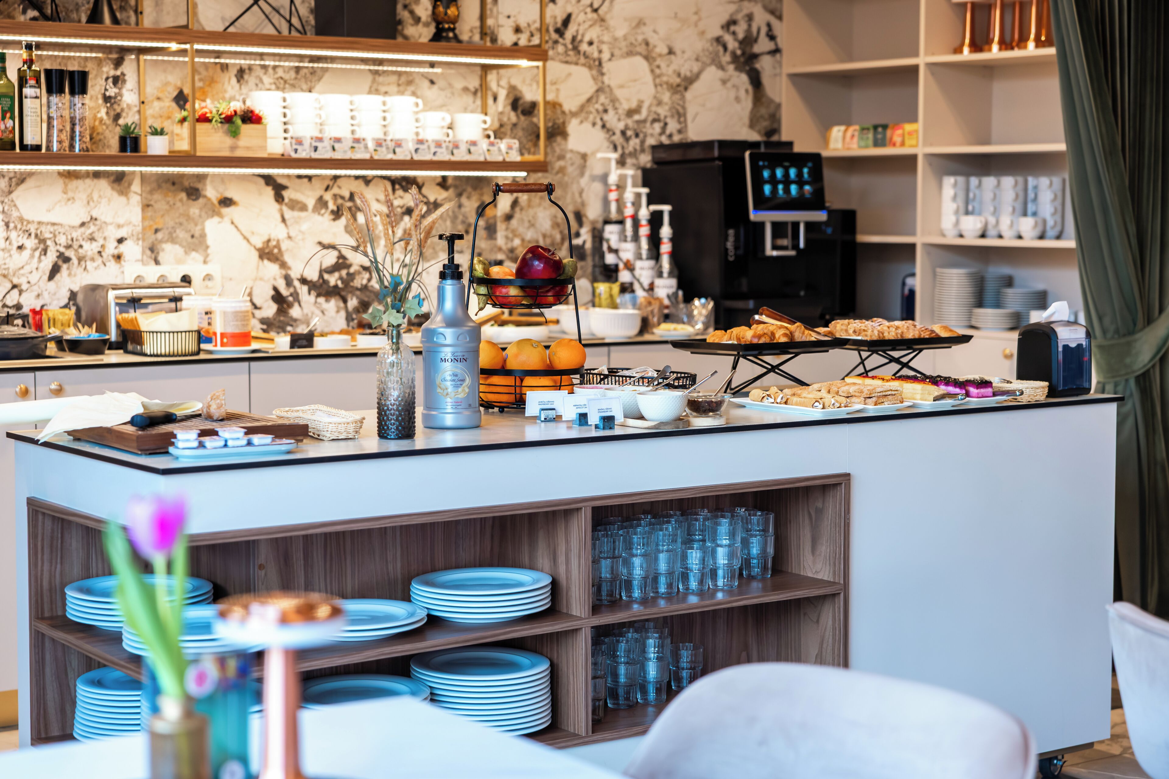 Una barra de desayuno con diferentes alimentos, una máquina de café y una selección de platos y vasos.