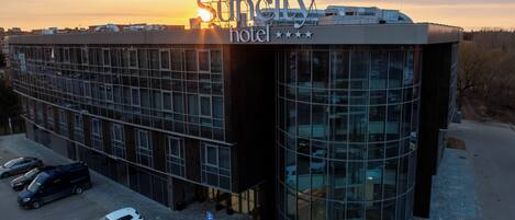Un moderno edificio de hotel con fachada de vidrio, un estacionamiento con varios coches y un cielo despejado al atardecer.