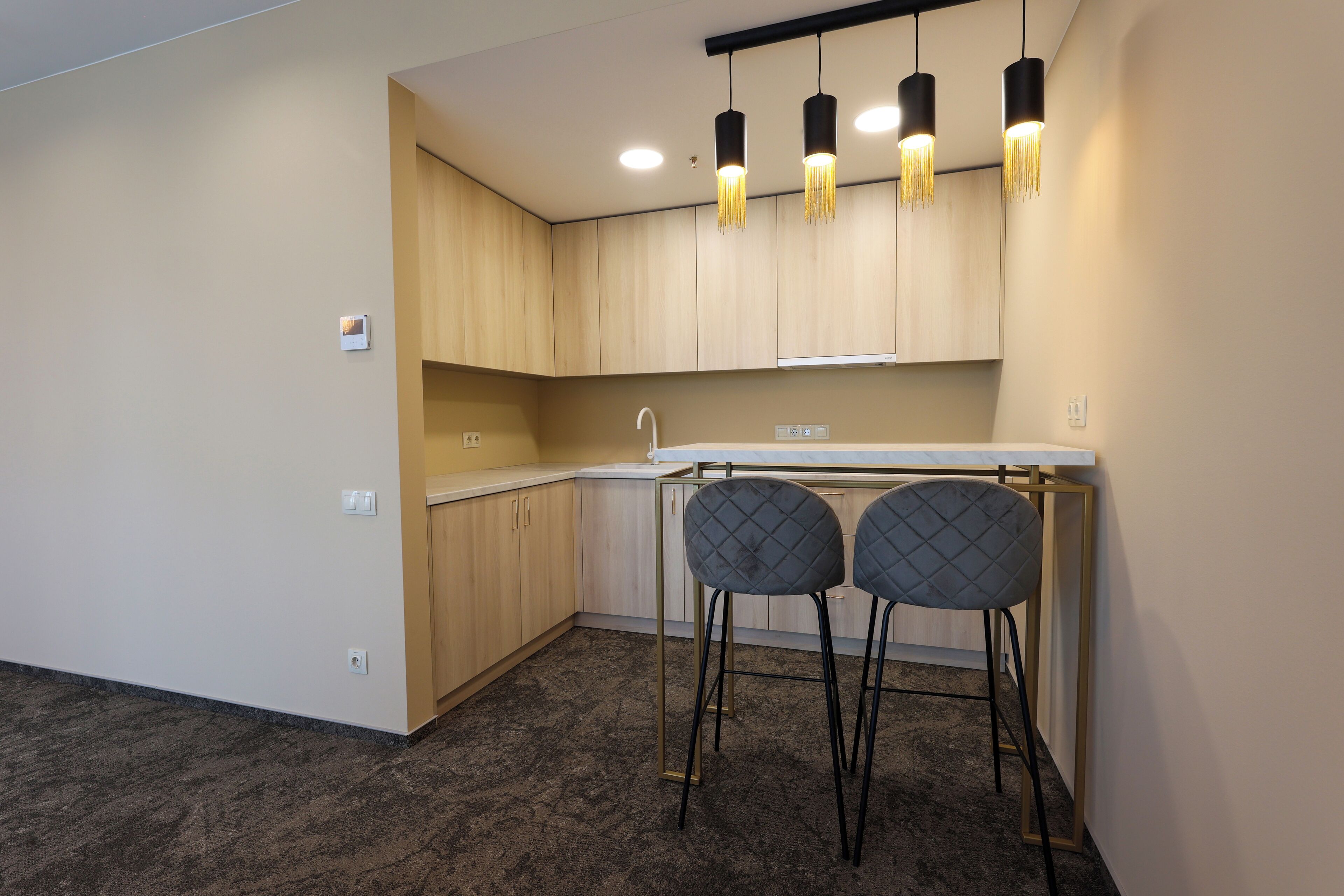 A modern kitchen with wooden cabinets, a white countertop, and two black bar stools.