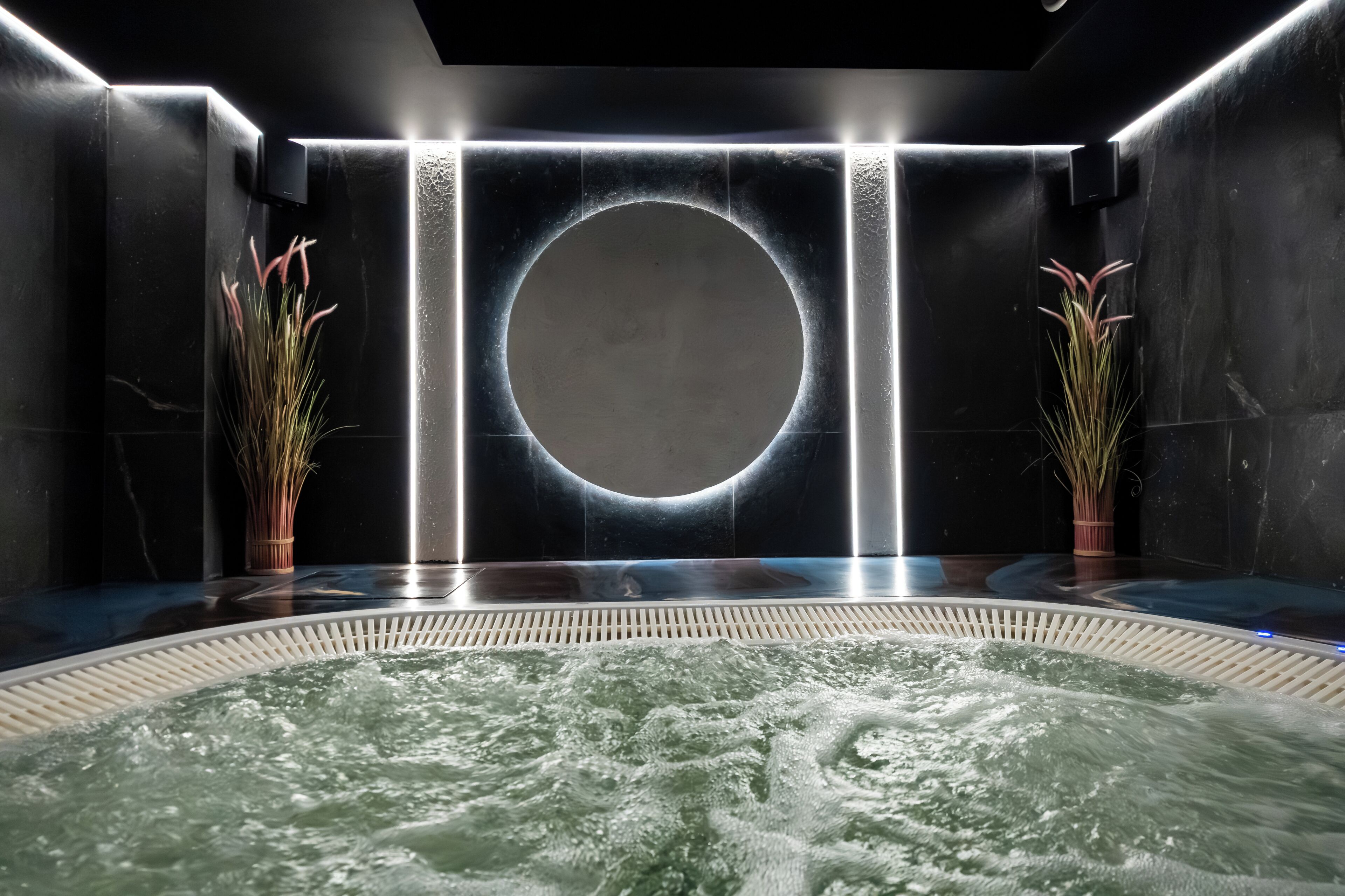 A spa area with a hot tub, dark walls, and two potted plants.
