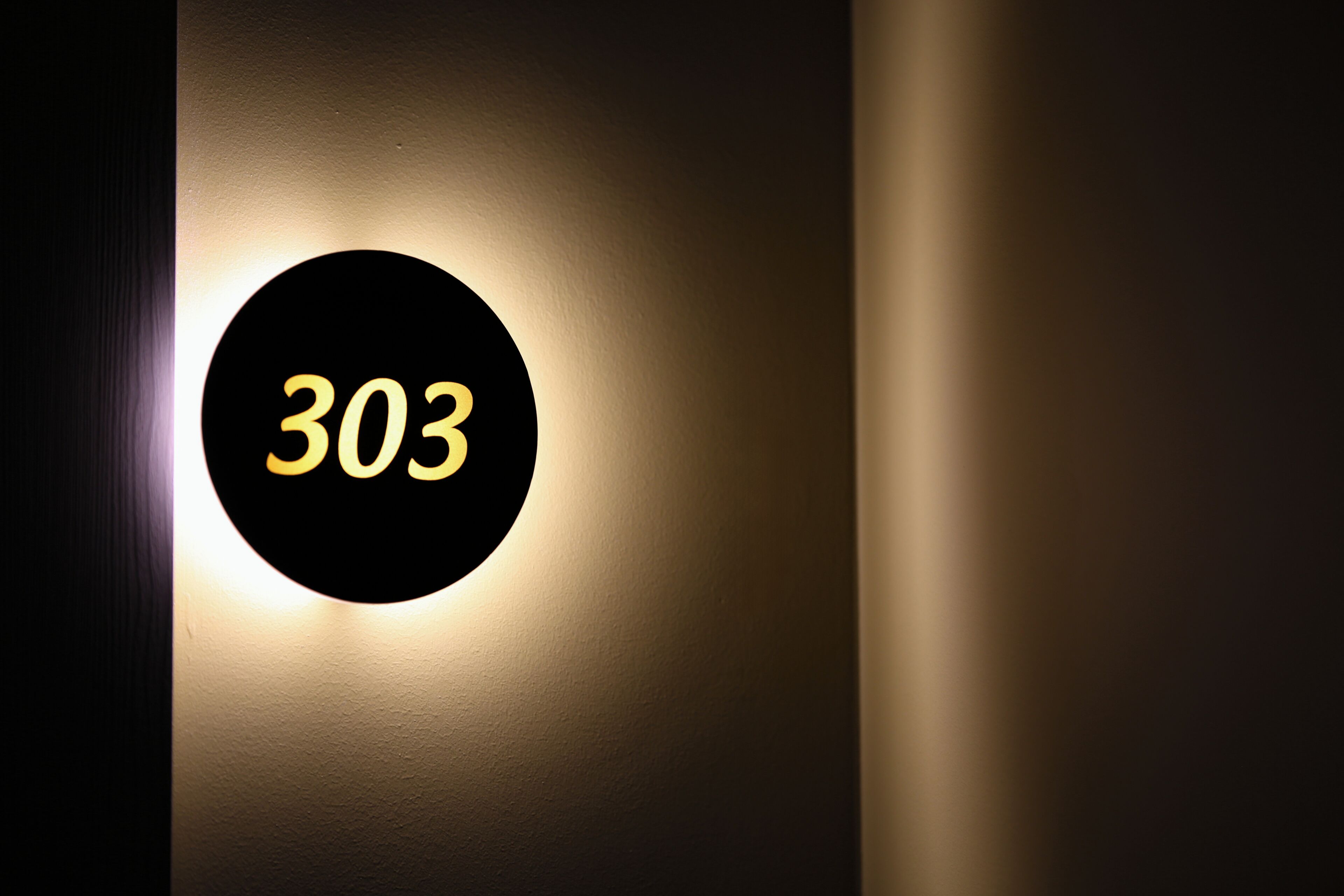 Una targa circolare fissata al muro con il numero 303 illuminato di giallo.