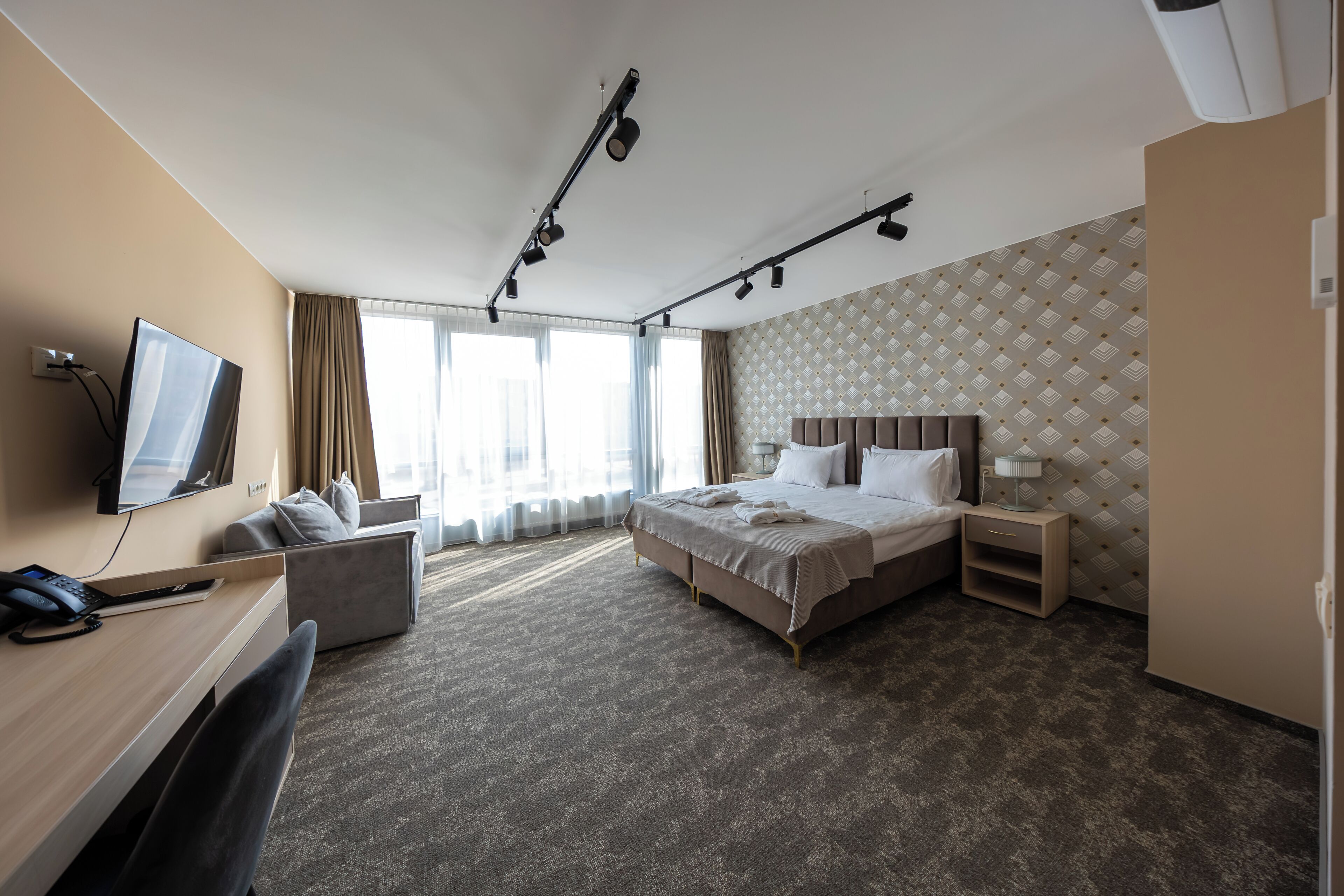 Ein Hotelzimmer mit Bett, Schreibtisch, Fernseher und einem großen Fenster mit Vorhängen.