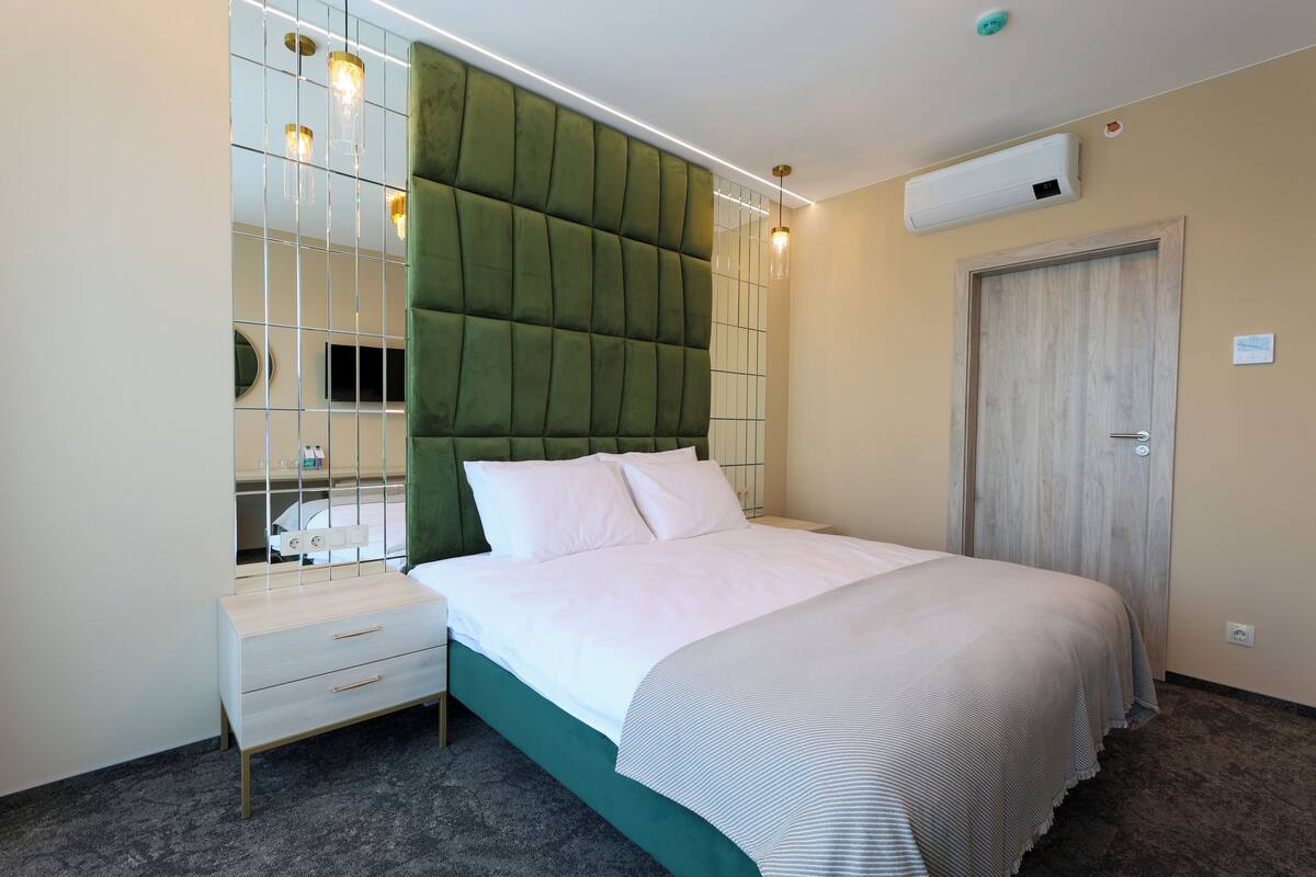 Ein modernes Hotelzimmer mit einem großen Bett, einem Nachttisch, einem Spiegel und einem Kleiderschrank.