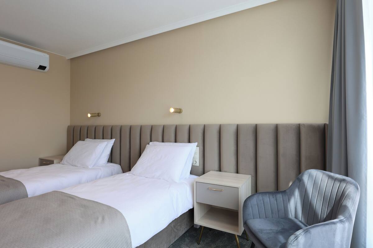Ein Hotelzimmer mit zwei Betten, einem Nachttisch, einem Sessel und einer Wand-Klimaanlage.