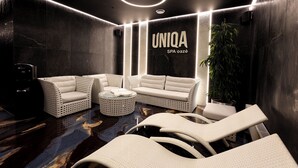 Een moderne spa-ruimte met een zwarte marmeren vloer, witte rieten meubels en een grote potplant.