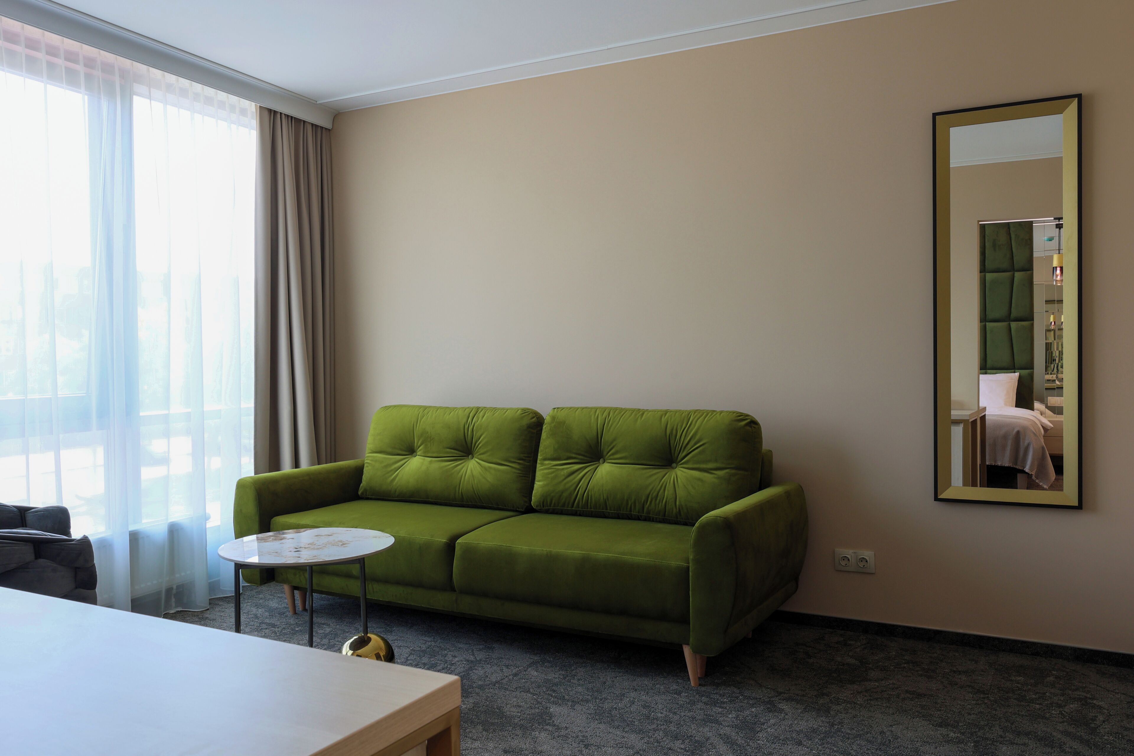 A green sofa, a round coffee table, a mirror, and a window with curtains.