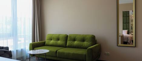 A green sofa, a round coffee table, a mirror, and a window with curtains.