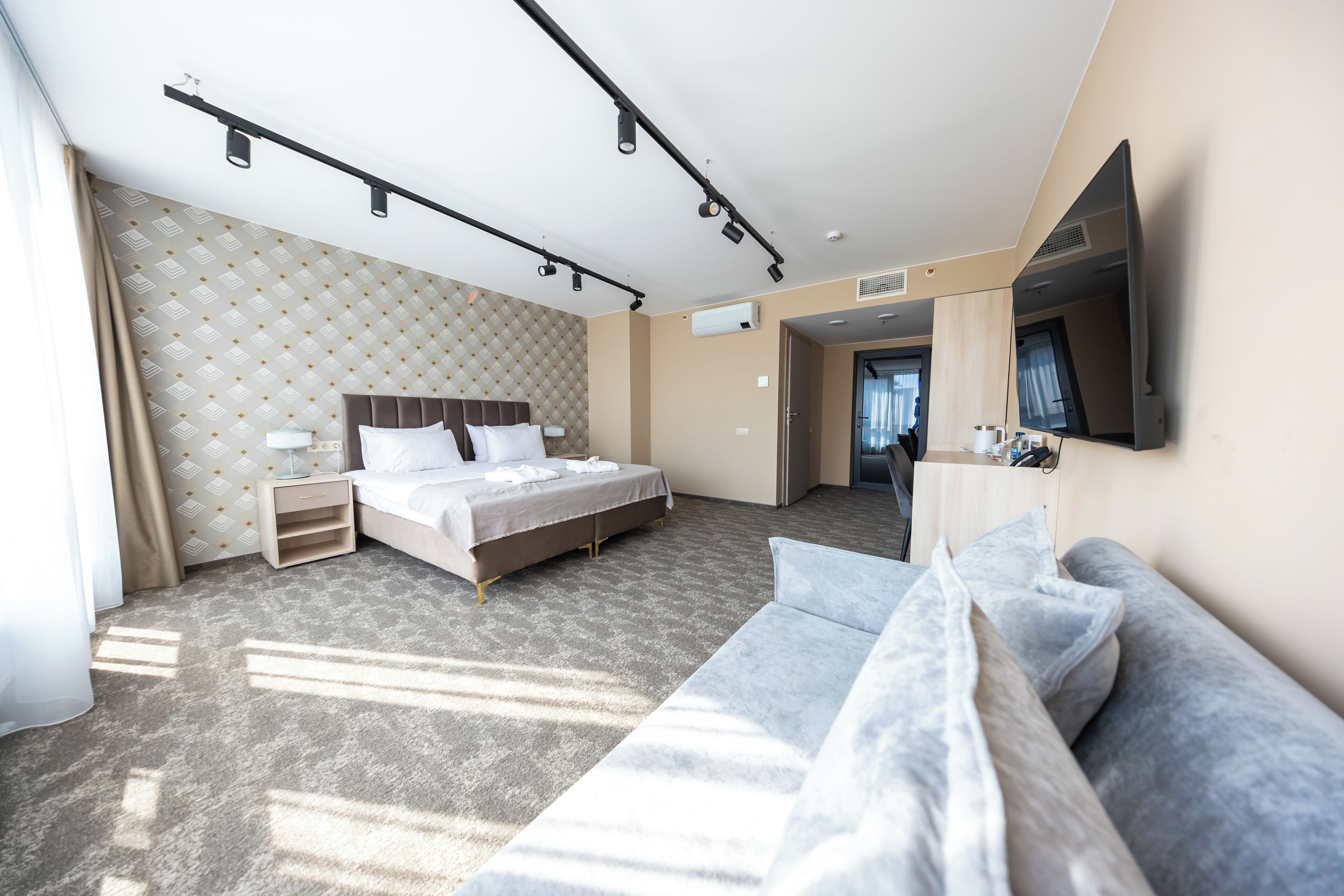 A modern hotel room with a large bed, a sofa, a flat-screen TV, and a walk-in closet.