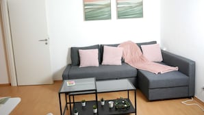 Una sala de estar con un sofá gris, dos mesitas pequeñas y una puerta blanca.