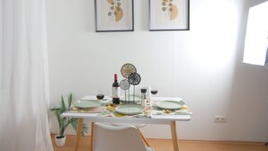 Una mesa de comedor dispuesta con platos, vasos, cubiertos, una botella de vino y una planta en maceta.