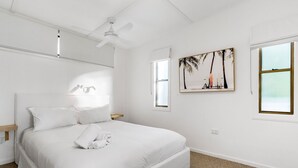 Ein helles Schlafzimmer mit Bett, Deckenventilator, Fenster und einem an der Wand hängenden Bild.