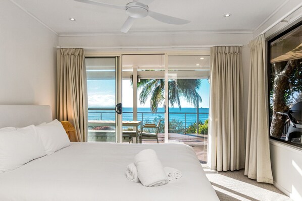 A hotel room with a large bed, a ceiling fan, and a view of the ocean through a sliding glass door.