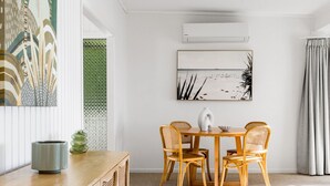 Ein Essbereich mit einem Holztisch, vier Korbstühlen, einer grünen Vase und einem Bild an der Wand.