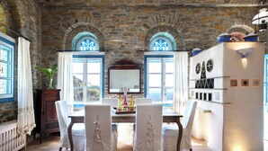 Un coin repas avec un mur en pierre, deux fenêtres en arc de cercle, une table avec des chaises et un réfrigérateur.