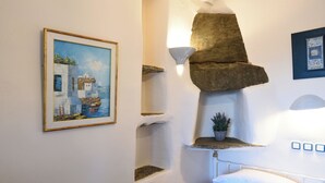 Une chambre à coucher avec un lit, un tableau représentant un paysage côtier, une étagère en pierre avec une plante et un luminaire fixé au mur.