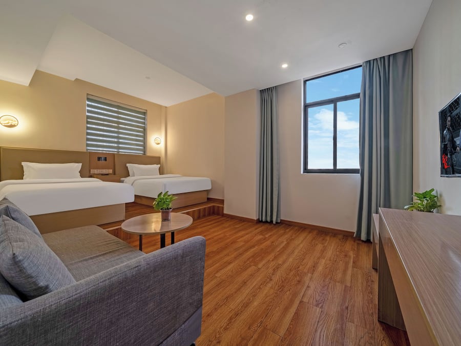 Quarto de hotel com duas camas, um sofá, uma mesa pequena e uma janela grande.