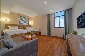 A hotel room with two beds, a sofa, a small table, and a large window.