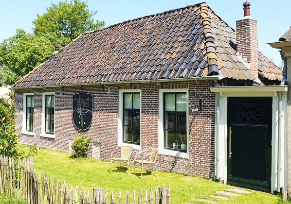 A brick house with a tiled roof, a front door, and a small garden with a wooden fence.