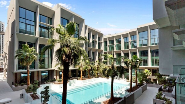 A modern hotel with a central swimming pool, surrounded by palm trees and lounge areas. - Vibrant & Exclusive Pool View Studio in Autograph (Dubai)
