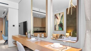 A modern dining area with a wooden table, chairs, and a large mirror reflecting the room. - Vibrant & Exclusive Pool View Studio in Autograph (Dubai)