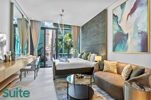 Una suite de hotel moderna con cama, sofá, comedor y un amplio ventanal con vista a la ciudad.
