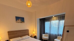 A hotel room with a large bed, two bedside tables with lamps, a chair, a window with curtains, and a painting on the wall. - Kırçak Konak (Cesme)