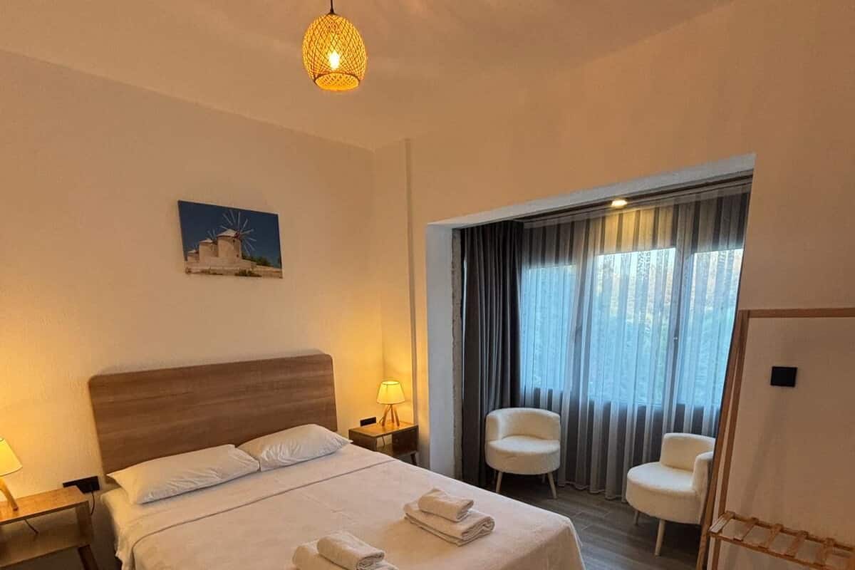 Une chambre d’hôtel avec un grand lit, deux tables de chevet avec des lampes, une chaise, une fenêtre avec des rideaux et un tableau au mur.