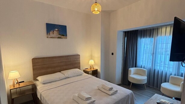 Ein Hotelzimmer mit einem großen Bett, zwei Nachttischlampen, einem Schreibtisch mit Stuhl, einem Fernseher und einem Bild an der Wand.