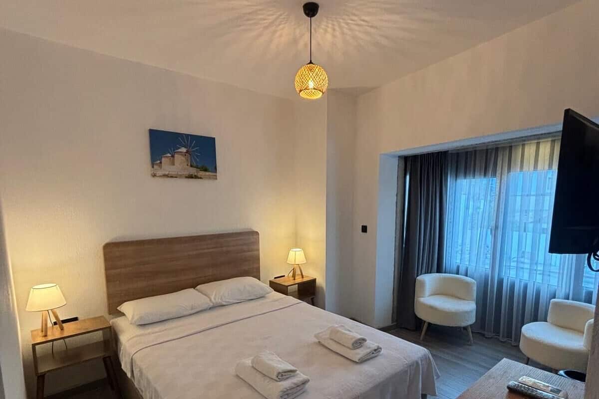 Une chambre d’hôtel avec un grand lit, deux lampes de chevet, un bureau avec une chaise, une télévision et un tableau au mur.