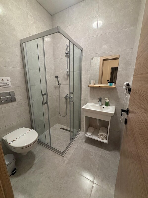 A modern bathroom with a glass-enclosed shower, a toilet, a sink with a mirror above, and a towel rack. - Kırçak Konak (Cesme)