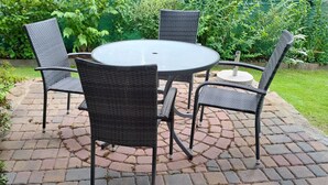 Uma mesa redonda com quatro cadeiras de vime num jardim.