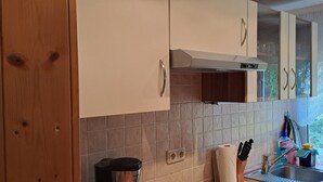 Uma cozinha com armários de madeira, coifa de aço inoxidável, painel de azulejos, janela com vista para o verde e pia com diversos utensílios.