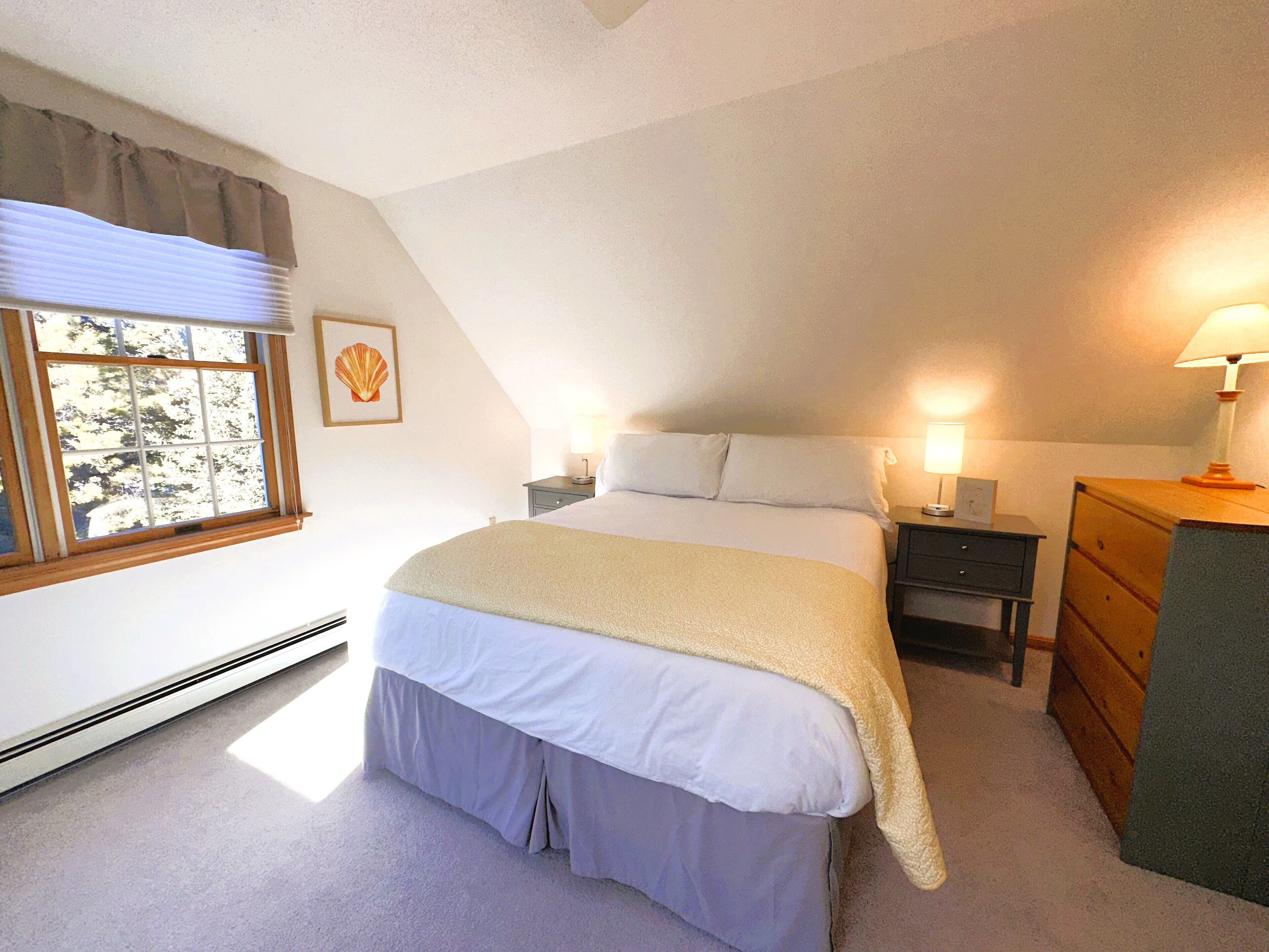 Een slaapkamer met een bed, nachtkastjes, een dressoir, een raam met uitzicht en een plafondventilator.