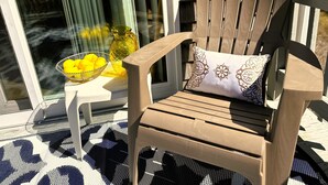 Une chaise en bois avec un coussin, placée sur un balcon d’où l’on peut admirer un bâtiment et une fenêtre.