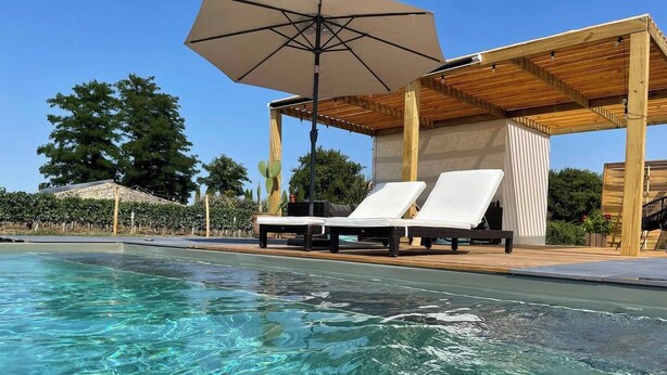 Ein klares Schwimmbecken mit Liegestühlen und einer Holzpergola mit Sonnenschirm.