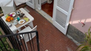 Une terrasse avec une table dressée pour deux personnes, protégée par un parasol blanc, et un escalier menant au niveau inférieur.