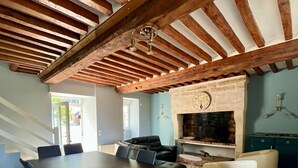 Una habitació àmplia amb un gran menjador, cadires blaves, una llar de foc i una paret de pedra amb un rellotge.